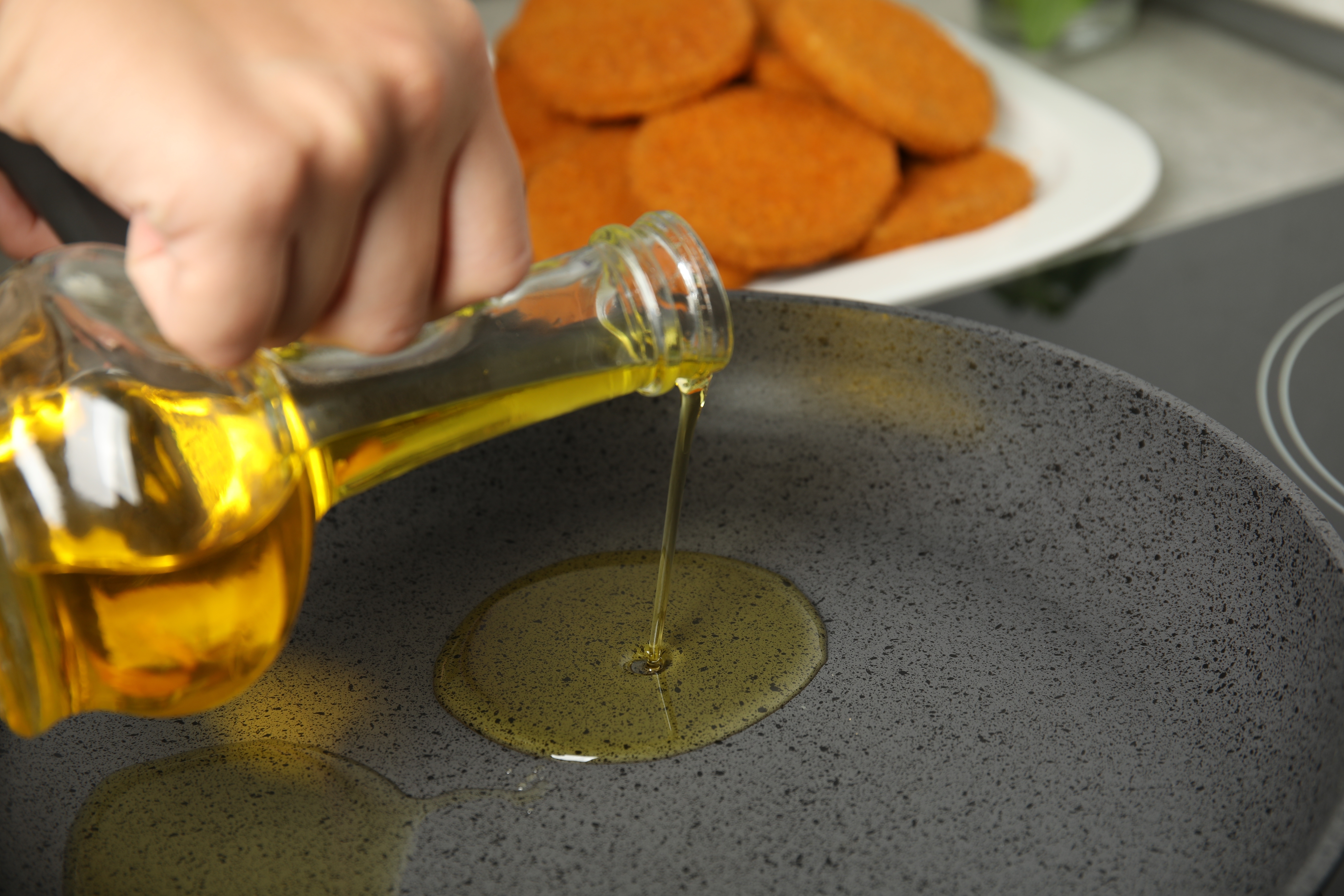 Woman adding oil on frying pan, closeup. Cooking breaded cutlets